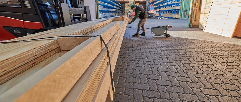 Mitarbeiter im Holzhandel mit Schubkarre beim Be- oder Entladen von langen Holzleisten im Außenlager.