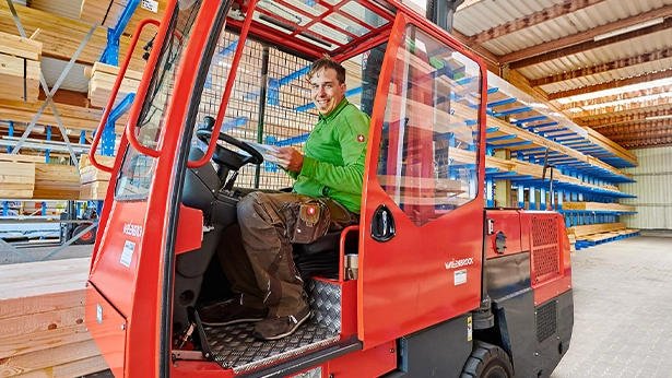 Mitarbeiter im Seitenstapler fährt durch das Lager mit freundlichem Blick – effizientes Lagermanagement.