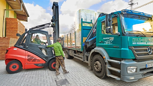 Mitarbeiter lädt mit Gabelstapler Materialien auf einen LKW – Logistik und Versand im Holzgroßhandel.