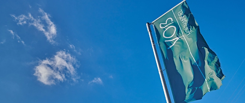 Fahne mit Voß Holzhandel-Logo weht im Wind vor blauem Himmel – Symbol für Qualität im Holzfachhandel.