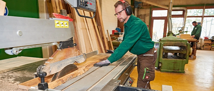 Facharbeiter an der Kreissäge beim exakten Zuschnitt eines Massivholzbretts – Handwerk mit Präzision.