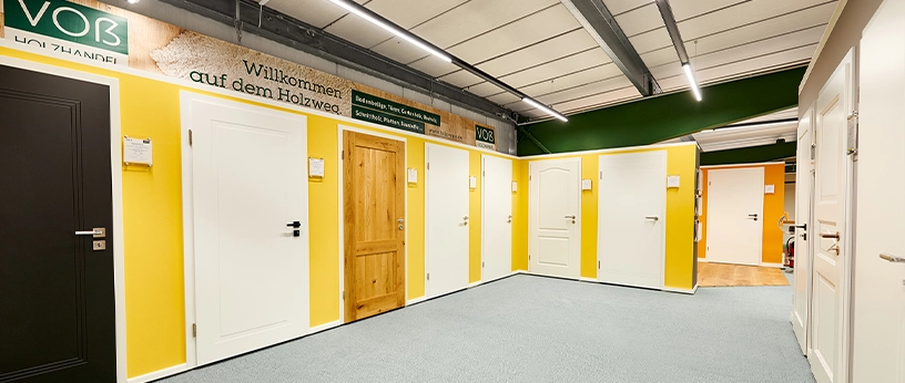 Türstudio mit gelber Wandgestaltung und großer Vielfalt an Türen – von schlicht bis rustikal mit Holzoptik.