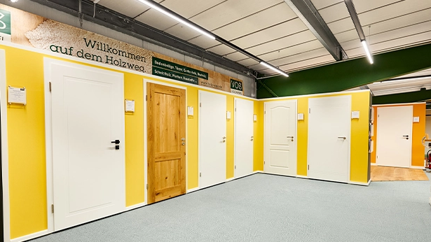 Türstudio mit gelber Wandgestaltung und großer Vielfalt an Türen – von schlicht bis rustikal mit Holzoptik.