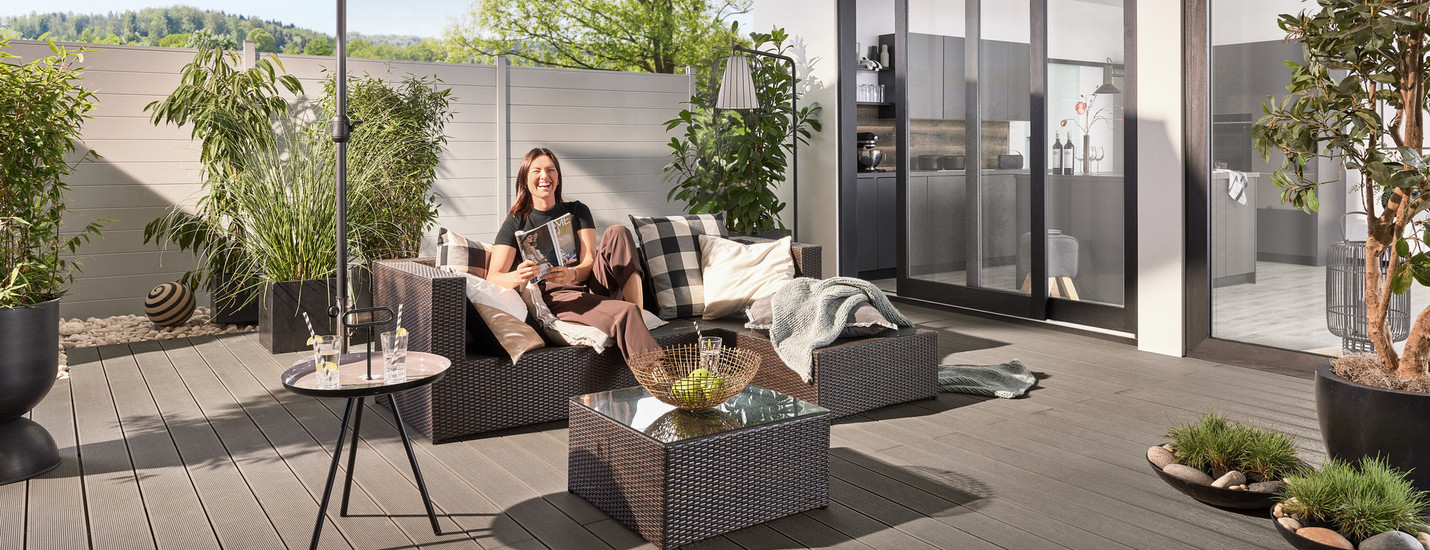 Schattiger Loungebereich auf moderner WPC-Terrasse mit Sonnenschirm und stilvollen Möbeln. Im Hintergrund WPC-Zaun.