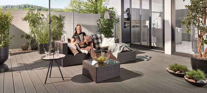 Schattiger Loungebereich auf moderner WPC-Terrasse mit Sonnenschirm und stilvollen Möbeln. Im Hintergrund WPC-Zaun.