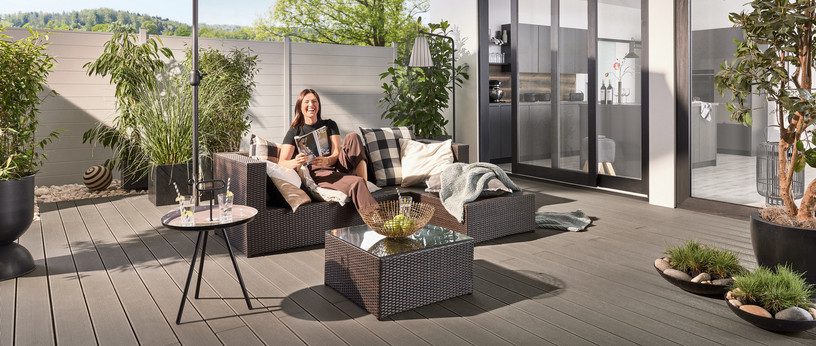 Schattiger Loungebereich auf moderner WPC-Terrasse mit Sonnenschirm und stilvollen Möbeln. Im Hintergrund WPC-Zaun.